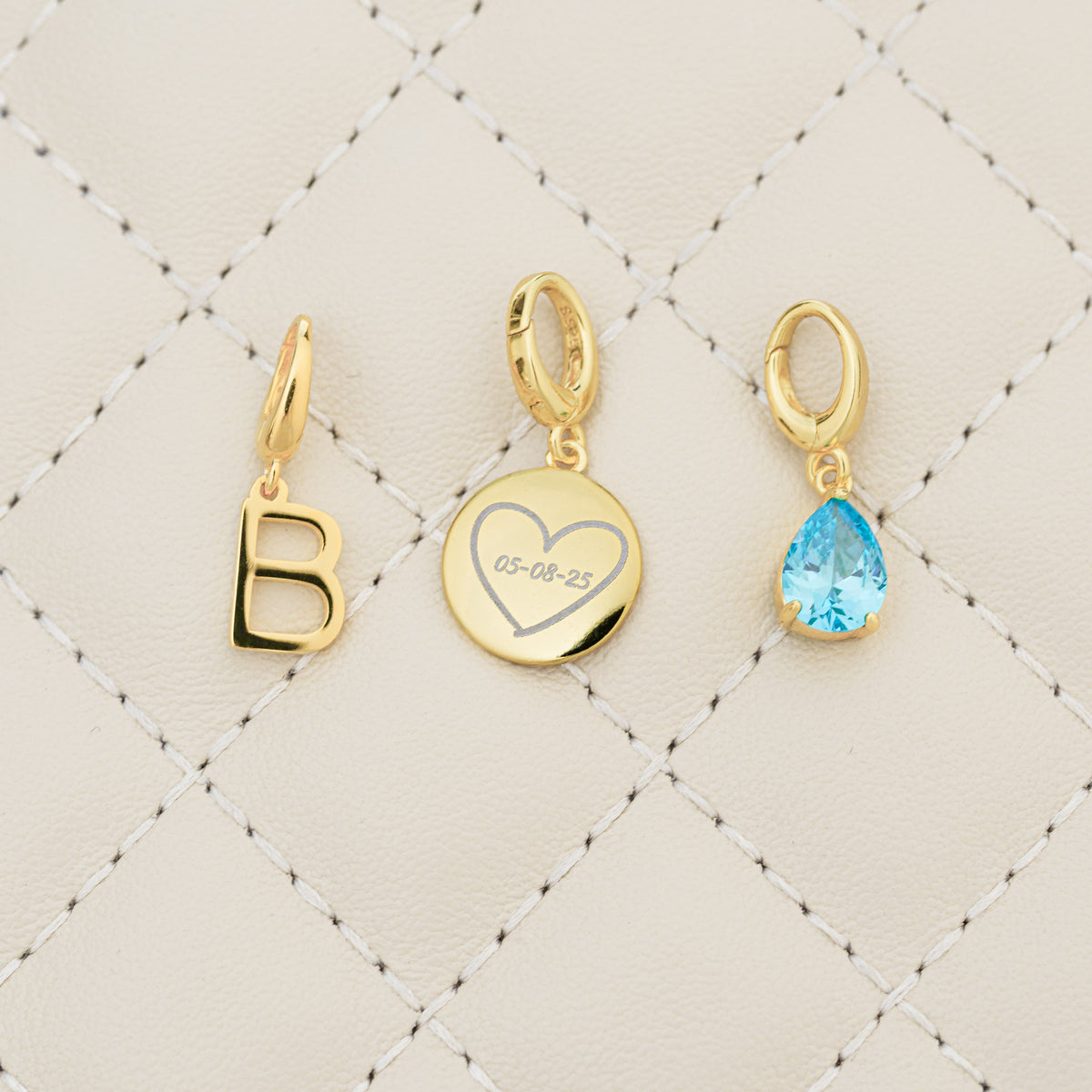 Three gold charms on a quilted beige background